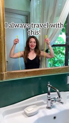 a woman standing in front of a bathroom mirror holding up two yellow hairdryers