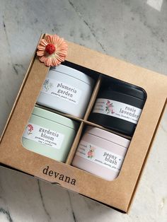 three jars of body lotion in a box on a marble surface with a pink flower