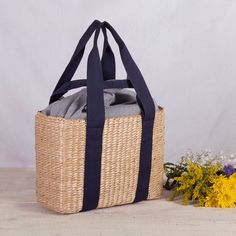 a large woven basket with black handles on a table next to flowers