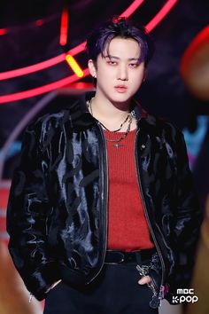 a young man with purple hair wearing a black jacket and red sweater standing in front of a neon sign