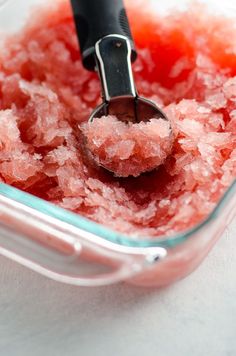 a bowl filled with pink sugar and a spoon in the center, on top of a white surface