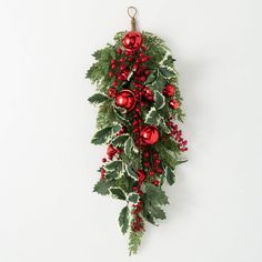 a red and green christmas decoration hanging on the wall with holly, balls and baubies