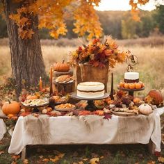 a table topped with cakes and desserts next to a tree filled with leaves in the fall