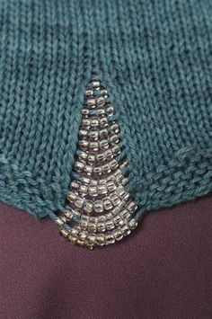 a close up view of a knitted sweater with beads on the bottom and side