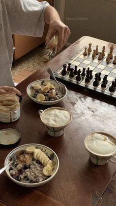 a man sitting at a table with several bowls of food on it, and chess in the background