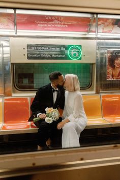 a man and woman sitting on a subway bench kissing in front of a train car