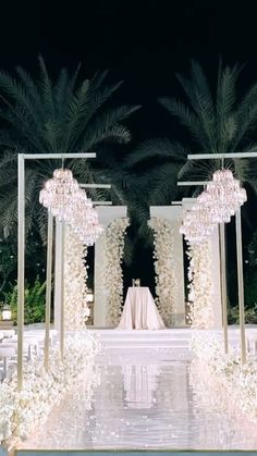 an outdoor wedding setup with white flowers and chandeliers on the side walk, surrounded by palm trees