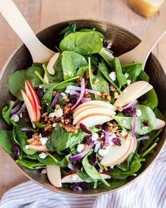 a salad with apples, spinach and walnuts in a bowl on a wooden table