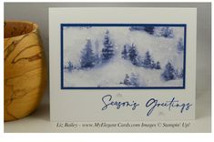 a greeting card with trees and snow on the ground in front of a wooden bowl