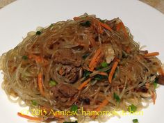 a white plate topped with noodles and meat on top of it's side next to green onions