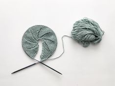 a ball of yarn next to a pair of knitting needles on a white surface with green yarn