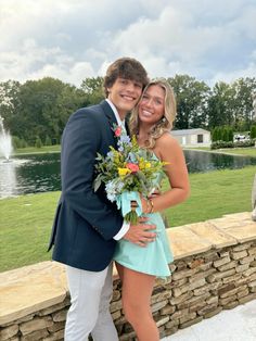 a young man and woman are posing for a photo in front of a fountain with flowers