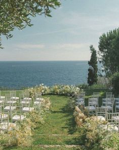 an outdoor ceremony set up with white chairs and flowers on the lawn by the ocean