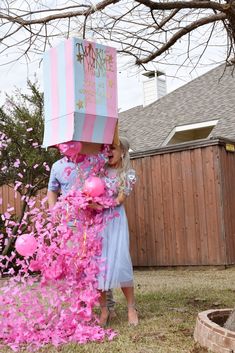 a woman in a blue dress is carrying a pink and white box on her head