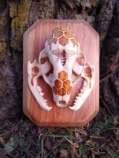 a carved animal head on a wooden plaque in front of a tree with grass and leaves