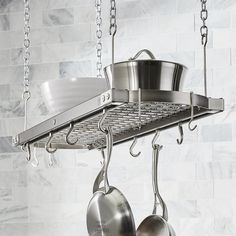 two pots and pans hanging from a rack in a kitchen with marble wall tiles