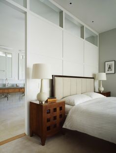 a white bed sitting next to two lamps on top of a wooden dresser in a bedroom