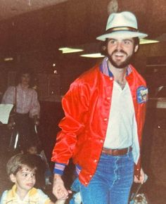 a man in a red jacket and hat holding hands with a little boy wearing blue jeans