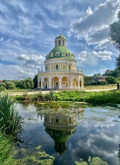 a large building with a green dome sitting on top of a lush green field next to a lake