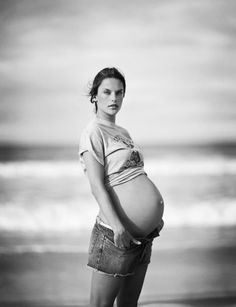 a pregnant woman standing on the beach with her belly wrapped around her waist and looking at the camera