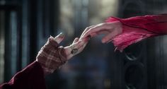 two hands reaching out towards each other in front of a black door with pink feathers on it