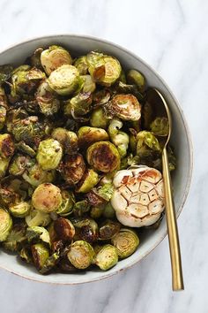 a bowl filled with brussel sprouts next to a golden spoon on a marble surface