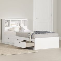 a white bed with drawers underneath it and a rug on the floor next to it