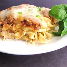 a white plate topped with pasta and meat covered in sauce next to spinach leaves