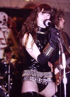 a woman singing into a microphone while holding a guitar in front of two other people