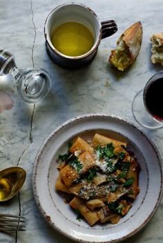 a white plate topped with pasta next to two cups of wine and bread on top of a table