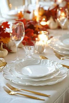 the table is set with white plates and silverware, gold place settings and candles