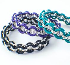 three different colored bracelets sitting next to each other on a white surface with silver and black links