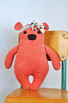 a pink teddy bear sitting on top of a wooden chair with a bow in it's hair