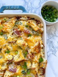 a casserole dish with ham, cheese and green onions in it next to a bowl of peas