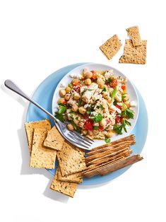 a white plate topped with pasta salad next to crackers and veggies on a blue plate