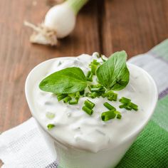 a small white bowl filled with sour cream and topped with fresh herbs on a green napkin