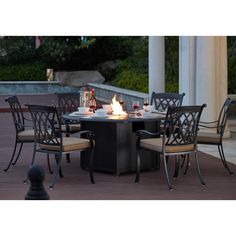 an outdoor dining table with chairs around it and lit candles on the fire pit area