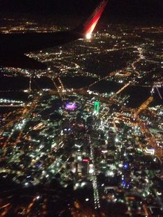 an airplane wing flying over a city at night with lights on the ground and buildings lit up