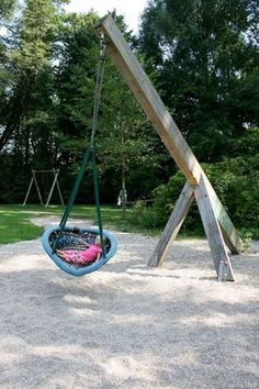 a swing set in the middle of a park with gravel and grass on it, surrounded by trees