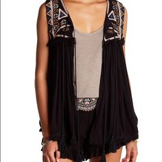 - Scoop Neck - Sleeveless - Double Front Tie Closure With Tassel Ends - Embroidered Front Yoke - Front And Back Fringed Yoke Trim - Allover Solid Gauze Construction - Fringed Reverse Hi-Lo Hem - Lined Yoke - Approx. 20" Shortest Length, 28" Longest Length (Size S) - Imported Fiber Content Shell: 100% Rayon Lining: 100% Cotton Dry Clean Only Additional Info Fit: This Style Fits True To Size. Model's Stats For Sizing: - Height 5'9'' - Bust: 31'' - Waist: 23'' - Hips: 34'' Model Is Wearing Size S Bohemian Black Embroidered Vest, Black Floral Embroidery Sleeveless Vest, Sleeveless Embroidered Top For Spring Festival, Spring Festival Embroidered Sleeveless Top, Bohemian Style Embroidered Vest For Summer, Black V-neck Embroidered Top For Summer, Bohemian Embroidered Vest For Summer, Black Tassel Tops For Summer, Black Summer Tops With Tassels