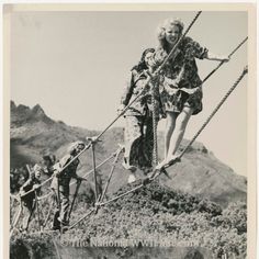 an old black and white photo of people walking across a rope bridge