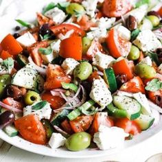 a salad with tomatoes, olives, cucumbers and feta cheese on a white plate