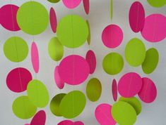 pink and green paper circles are hanging from strings on a white wall with string attached to it