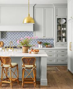 two chairs are sitting at the center of this kitchen island with gold pendant lights hanging over it