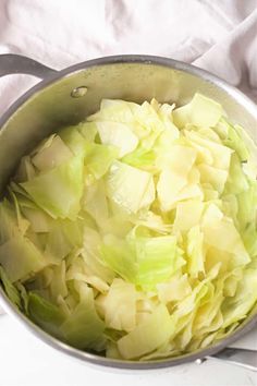 a pot filled with chopped cabbage on top of a white table cloth next to a knife