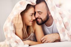 a man and woman laying in bed under a blanket smiling at each other with their eyes closed