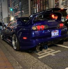 the back end of a blue sports car parked in front of a tall building at night