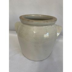 a large white vase sitting on top of a white cloth covered table next to a wall