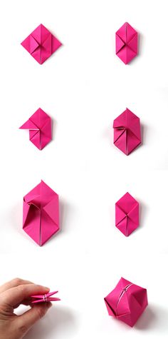 a hand holding a pink pen and some origami pieces on a white surface