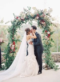 a bride and groom kissing in front of an arch with flowers on it at their wedding